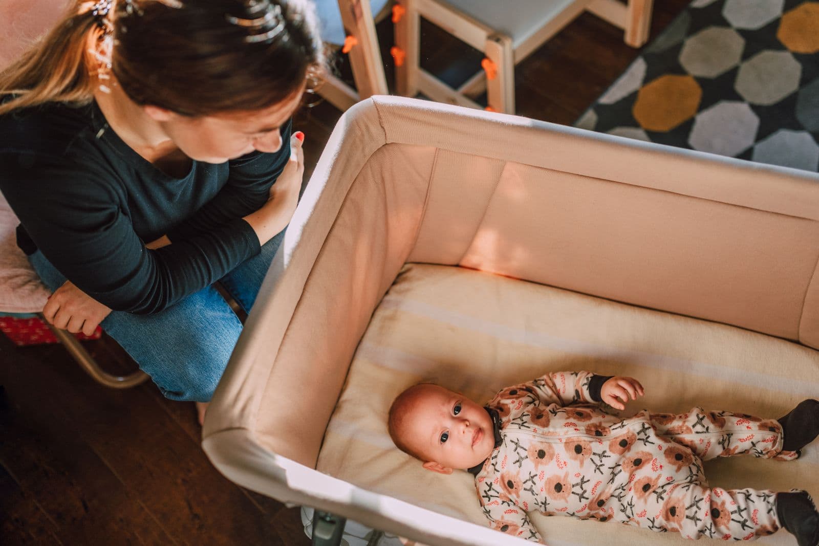 A mother leaning over a bassinet to check on her baby in a sunlit room