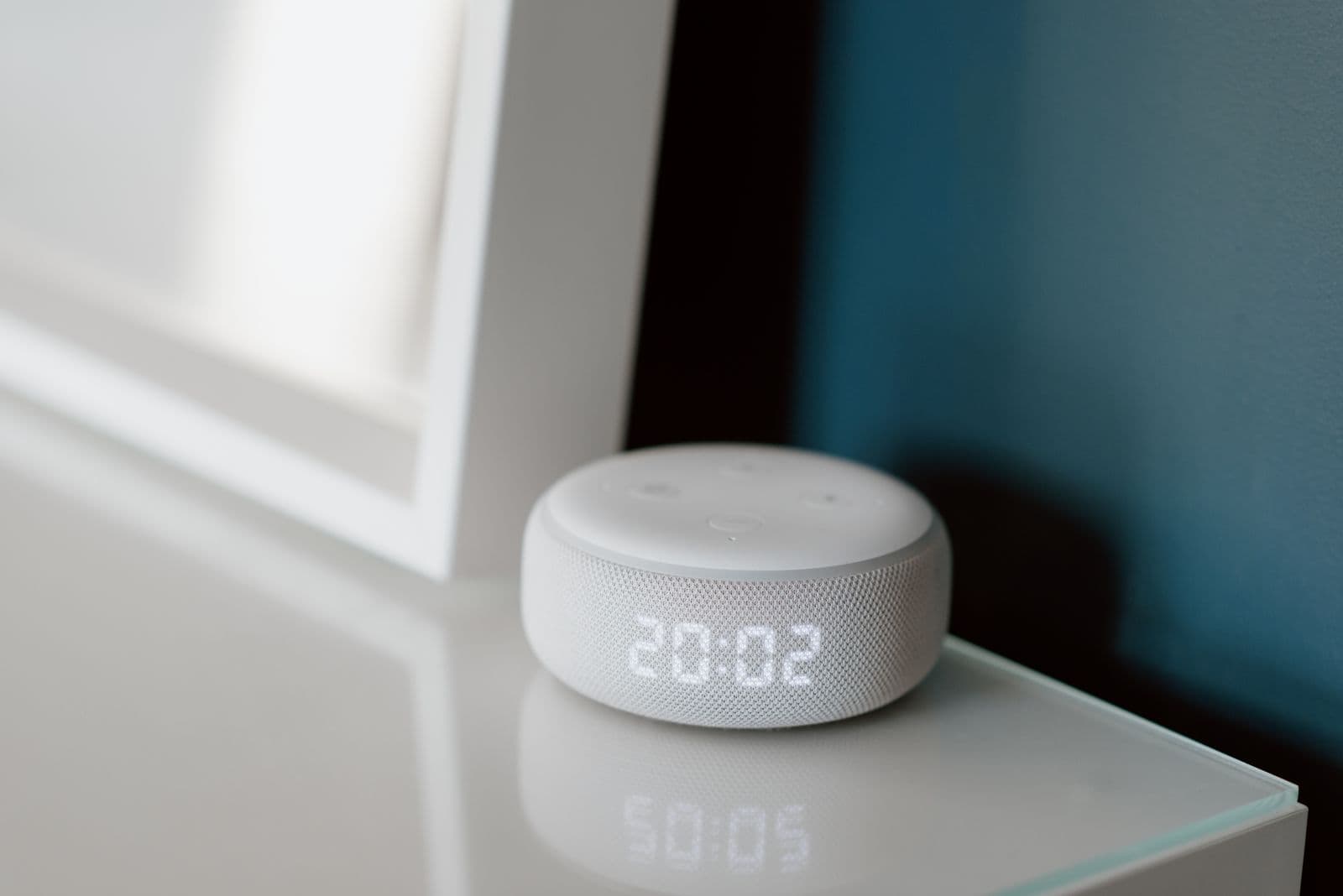A small smart speaker with an illuminated clock display on a bedside table