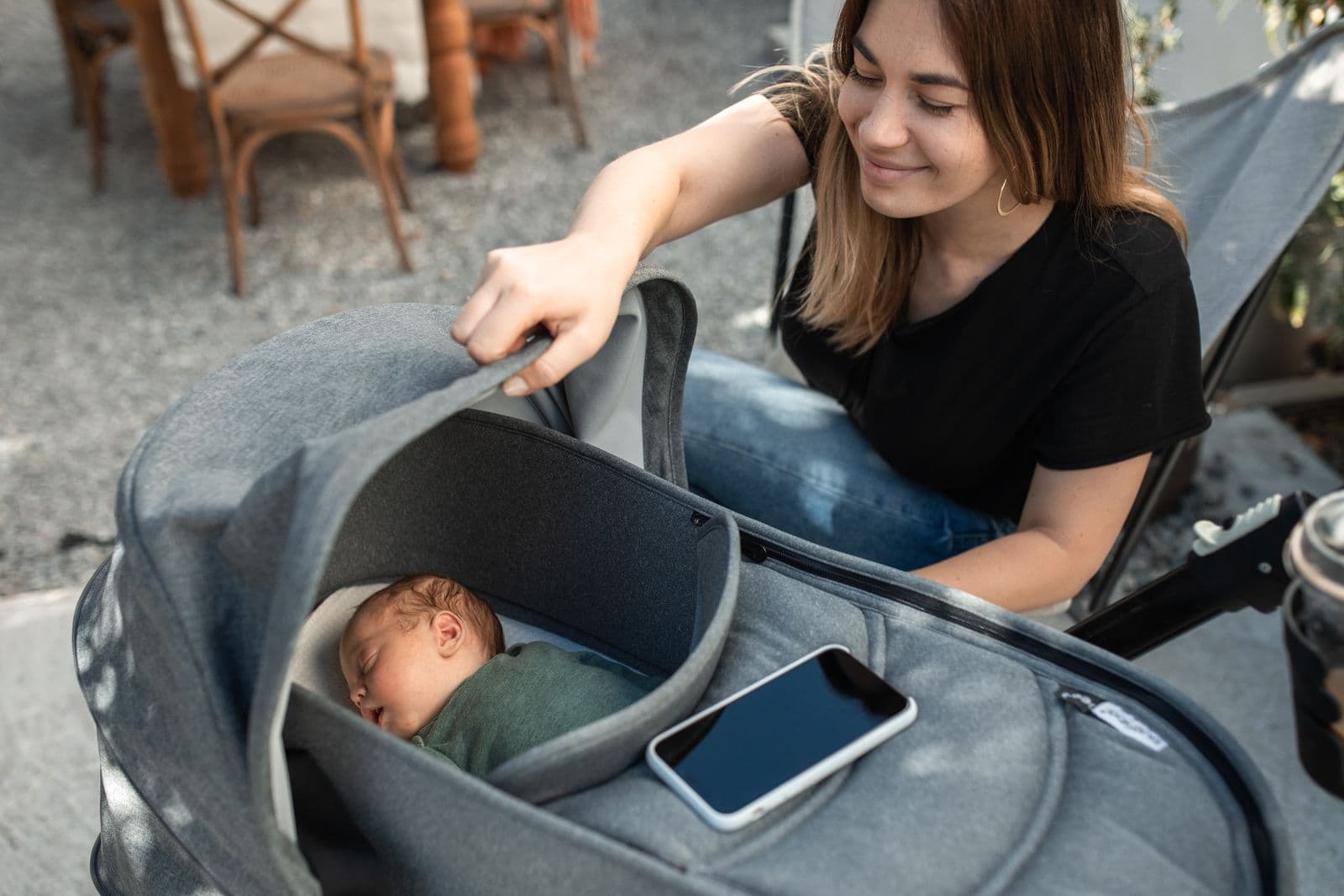 A parent lifting the canopy of a pram carrycot to check on a newborn asleep on its back