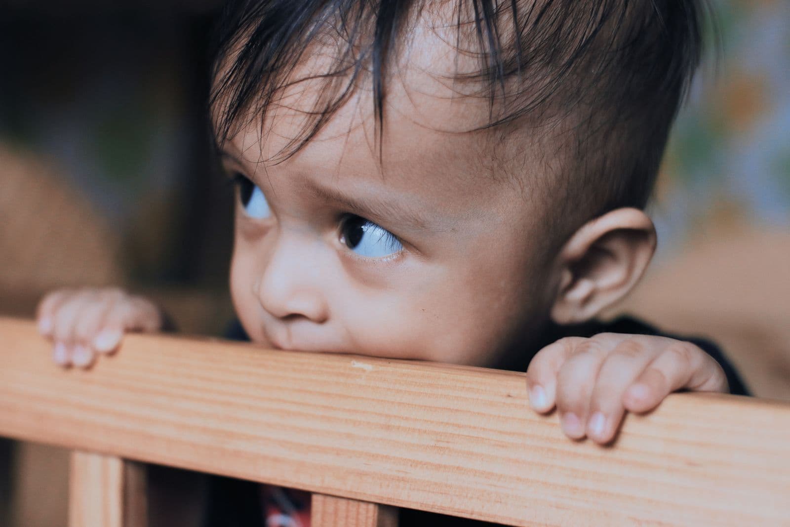 A toddler standing at a crib rail, gripping the top of it with both hands