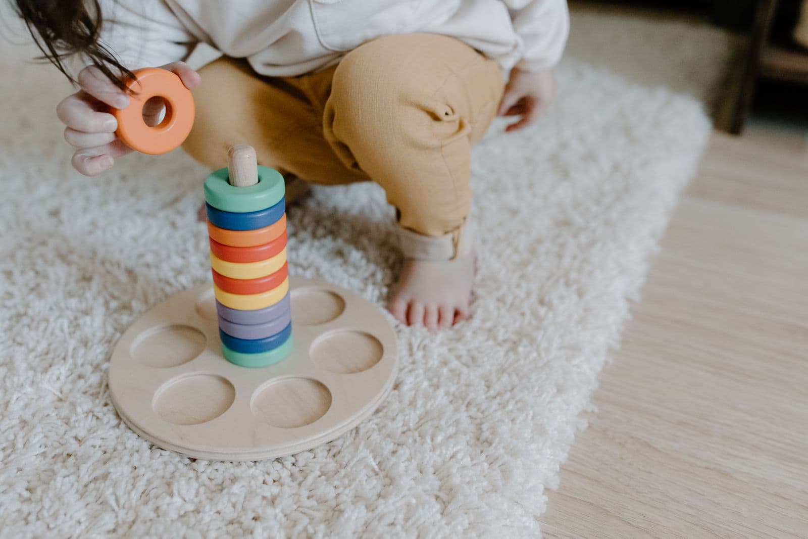 A child playing with a wooden ring stacking toy on a rug