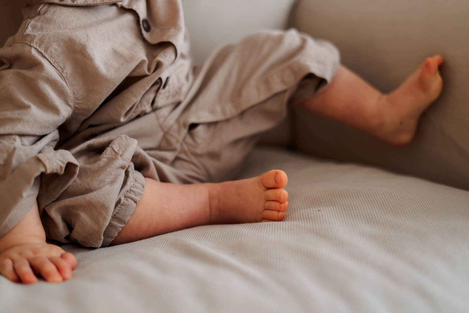 A baby's legs and bare feet as they sit on a sofa