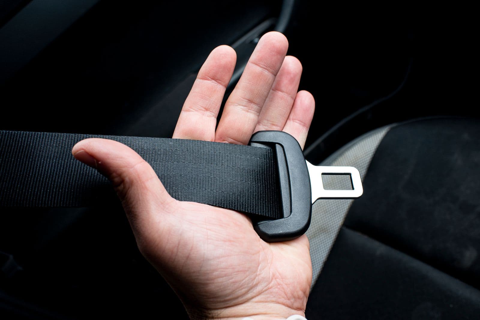 A hand holding a vehicle seat belt and its metal latch plate inside a car