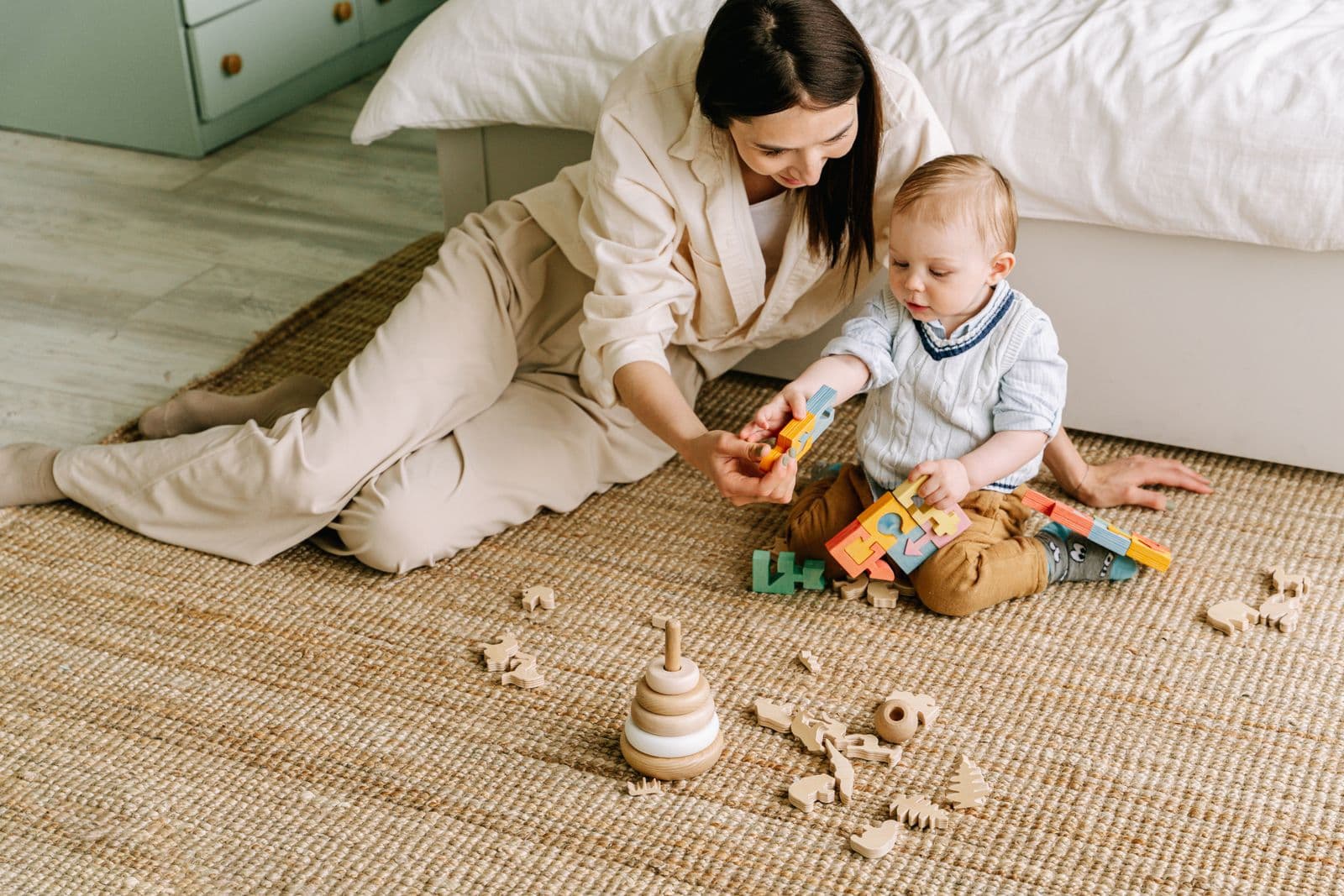 A parent and baby playing with wooden toys on a rug