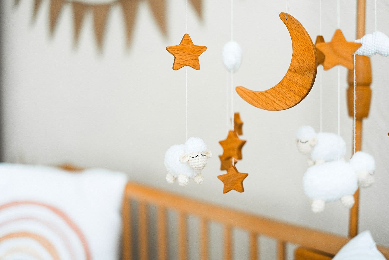 A wooden crib mobile of stars, a crescent moon and crocheted sheep hanging over the rail of a wooden crib